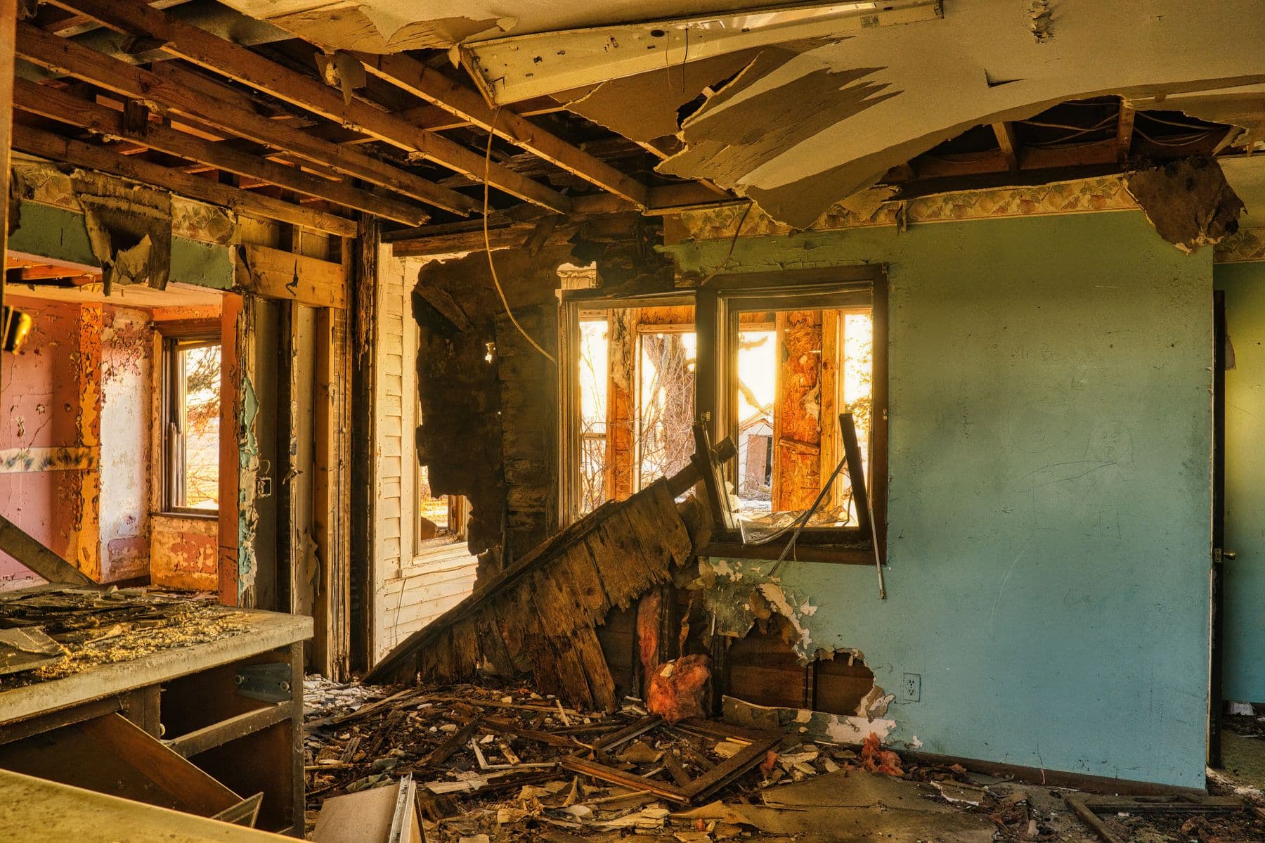 The inside of a house with the ceiling opened to the joists, walls broken through and debris on the floor.